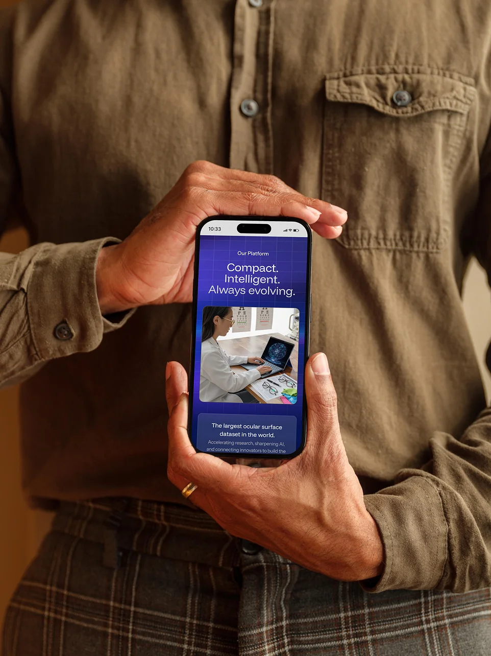 Person holding a smartphone displaying a platform with text about the largest ocular surface dataset, featuring an image of a woman examining eye charts.